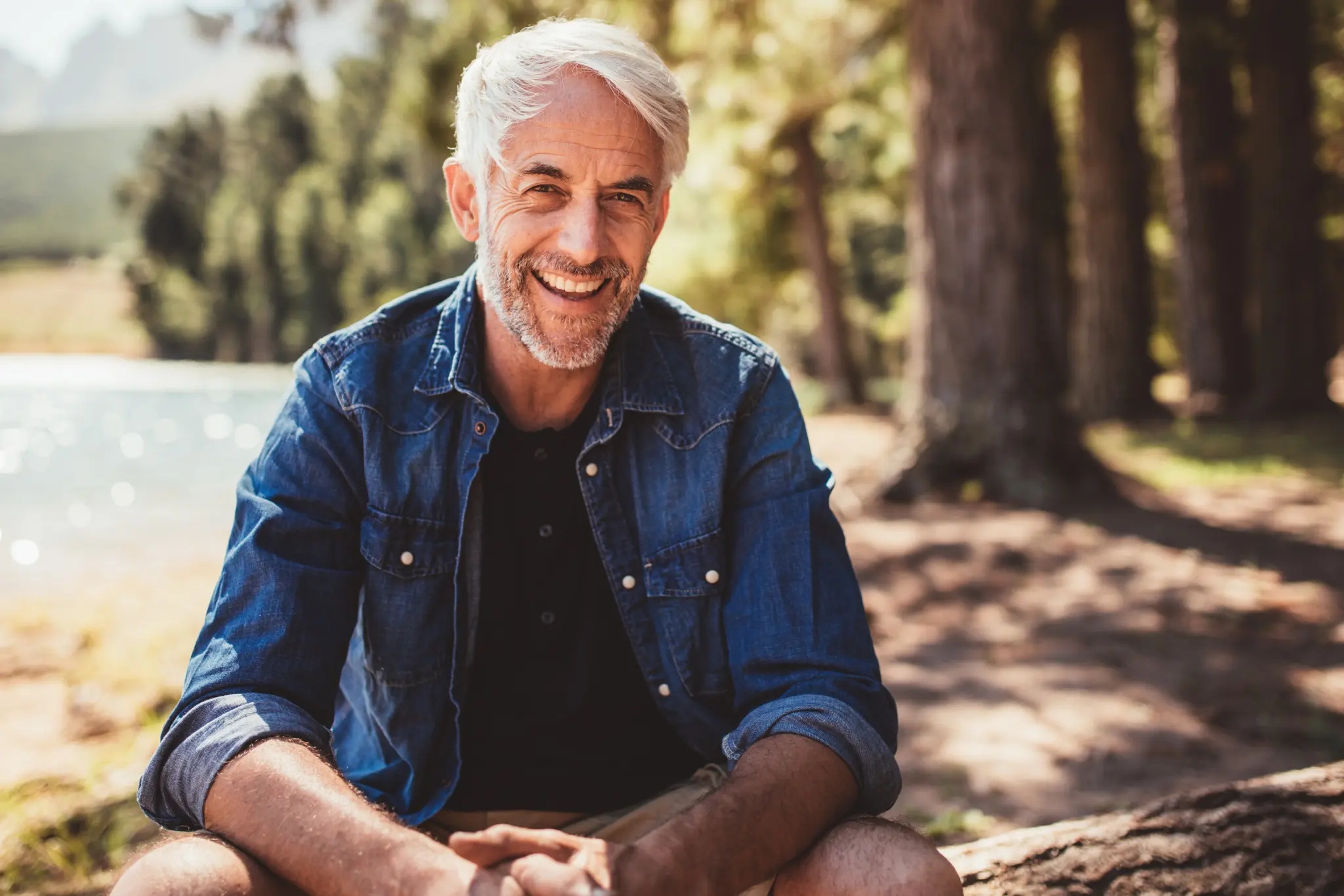 Smiling man sitting outdoors in nature.